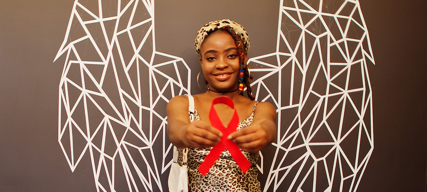 Smiling black woman with wings holding out a red ribbon signifying hiv awareness